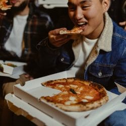 asian male eating pizza with friends at night