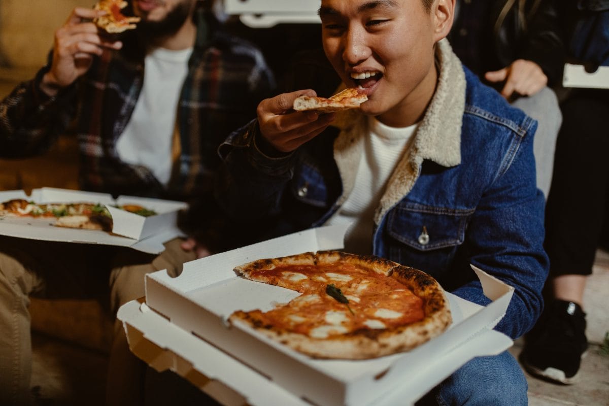 asian male eating pizza with friends at night